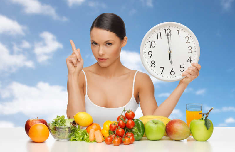 一桌子的蔬菜和水果还有一个拿着中钟表的女人