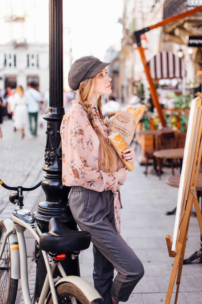 年轻的模特站在街上拿着面包带着自行车