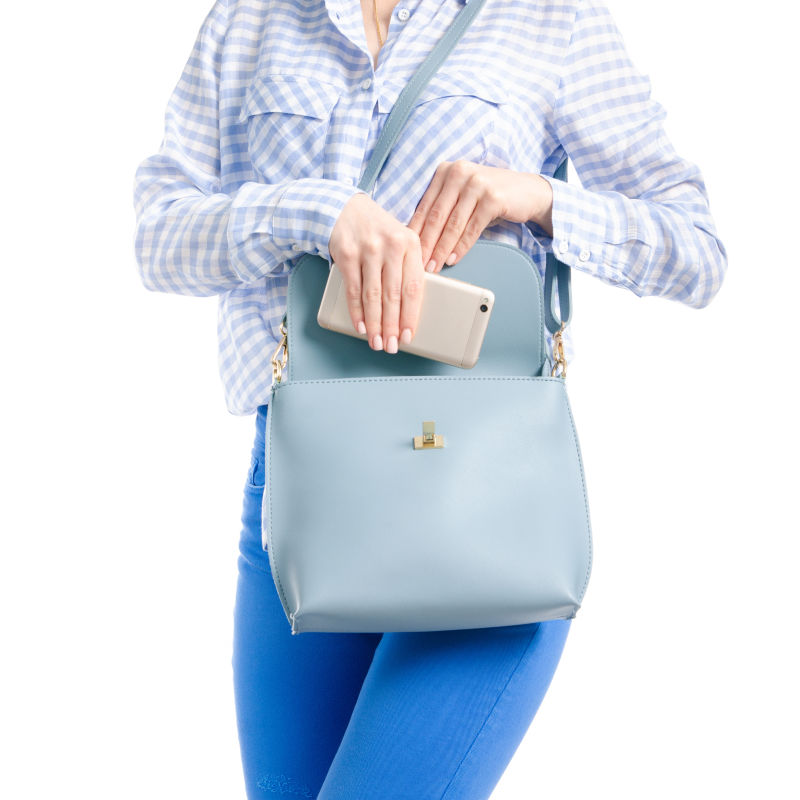穿牛仔裤和蓝色衬衫的女人把智能手机放在白色背景的蓝色袋子里