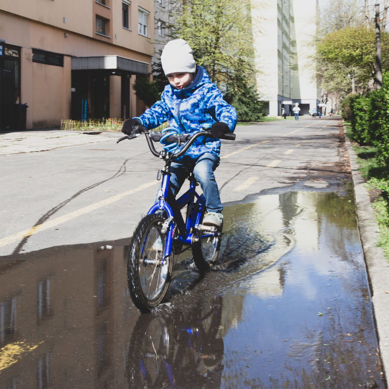 男孩骑着自行车穿过街上的水坑