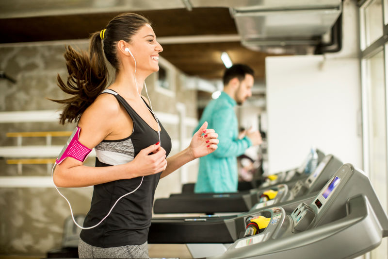 年轻女子在跑步机上跑步在健身房听音乐