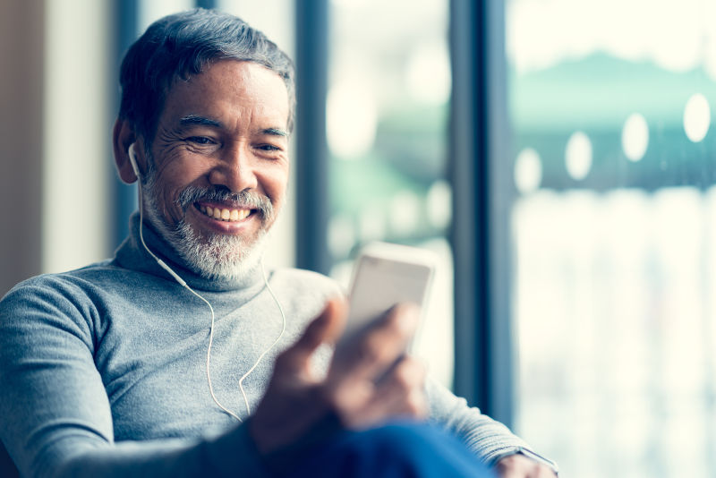 带着迷人微笑的成年男人退休了留着白色时髦的短胡须用智能手机或听音乐坐在咖啡馆咖啡厅通过他的小工具提供互联网服务老人使用社会