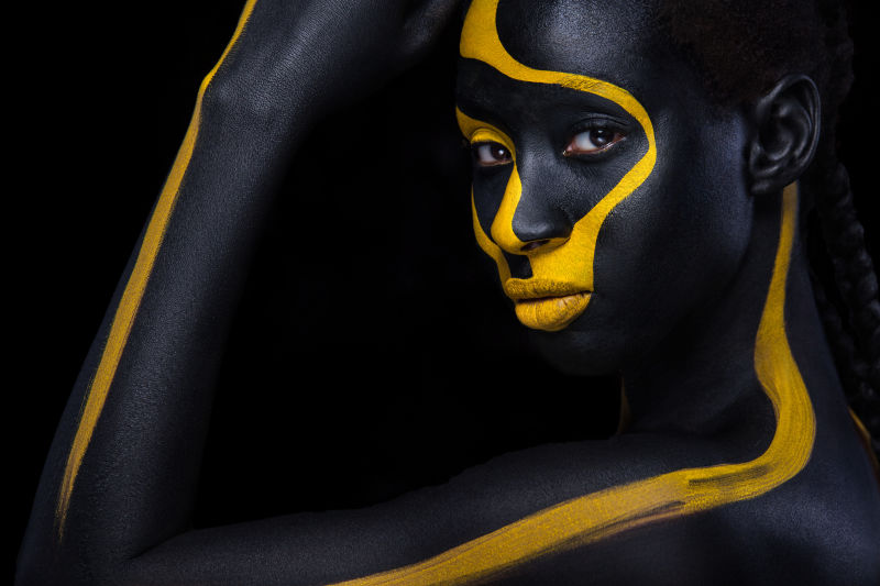 带着艺术时尚妆的快乐的非洲年轻女子一个有着黑色和黄色彩妆的神奇女人