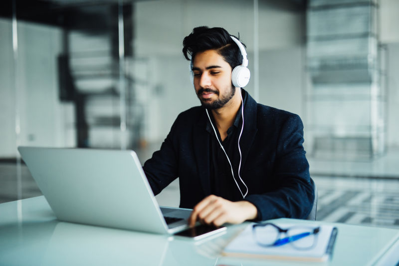 印度年轻商人戴着耳机手提电脑在办公室工作听音乐