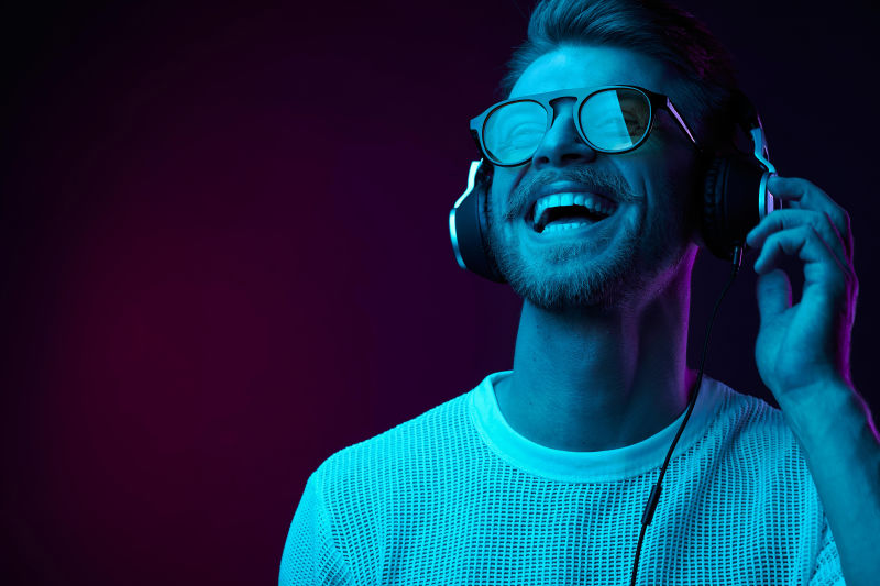 霓虹灯肖像戴着耳机太阳镜和白色T恤的胡须微笑的男人听音乐