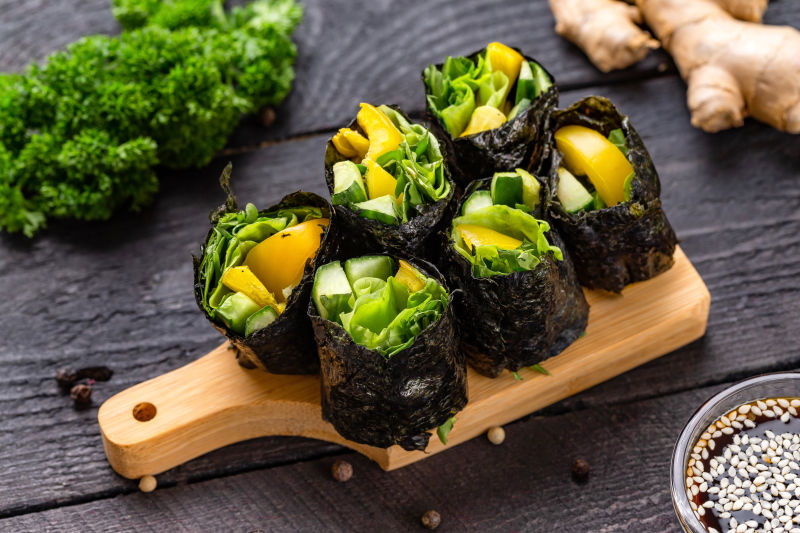 一套健康的素食寿司卷-配黄瓜胡椒和绿色色拉-以木桌为背景