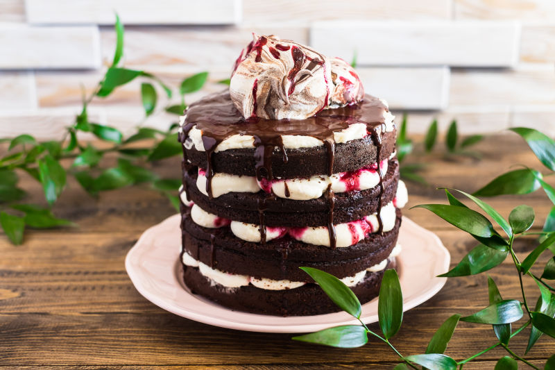 巧克力蛋糕称为黑森林蛋糕-配樱桃和巧克力酱-在木桌上的盘子上装饰着用甜蛋白酥皮装饰的奶油芝士