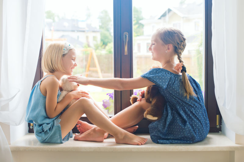 两个可爱的欧洲小女孩坐在靠近窗户的窗台上玩玩具