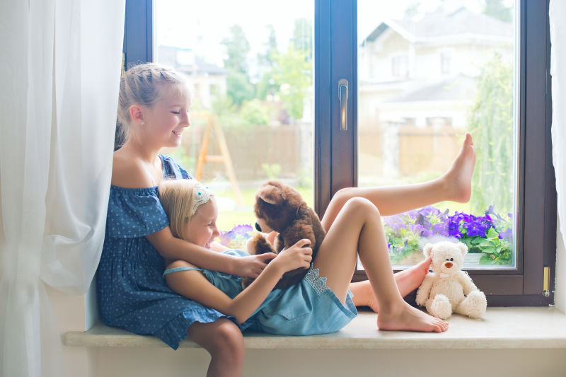 两个可爱的欧洲小女孩坐在靠近窗户的窗台上玩玩具