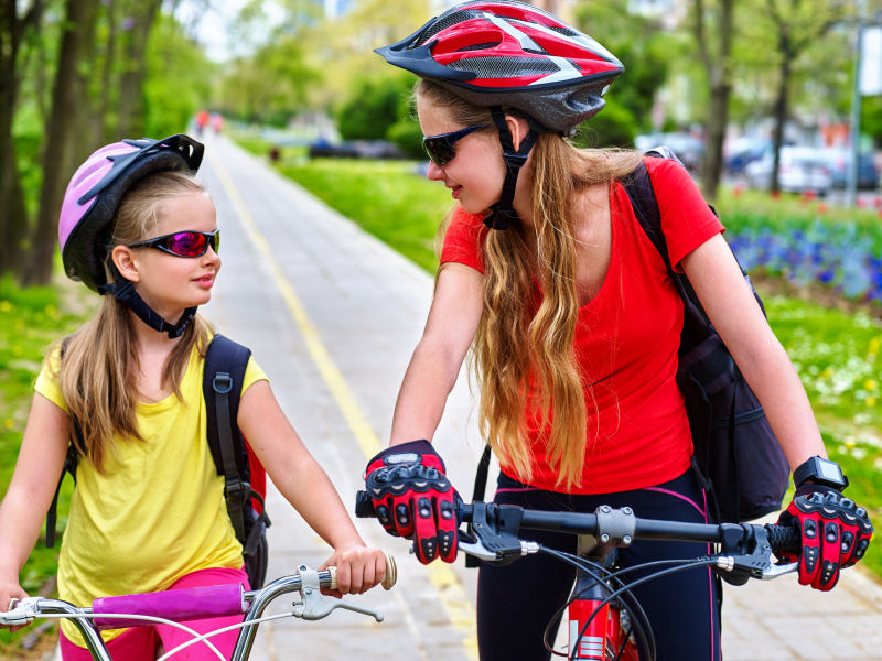 女孩们戴着自行车头盔和玻璃背着帆布包骑着自行车女童在黄色自行车道上骑车自行车共享计划节省了城市街道的金钱和时间女孩们互相交谈