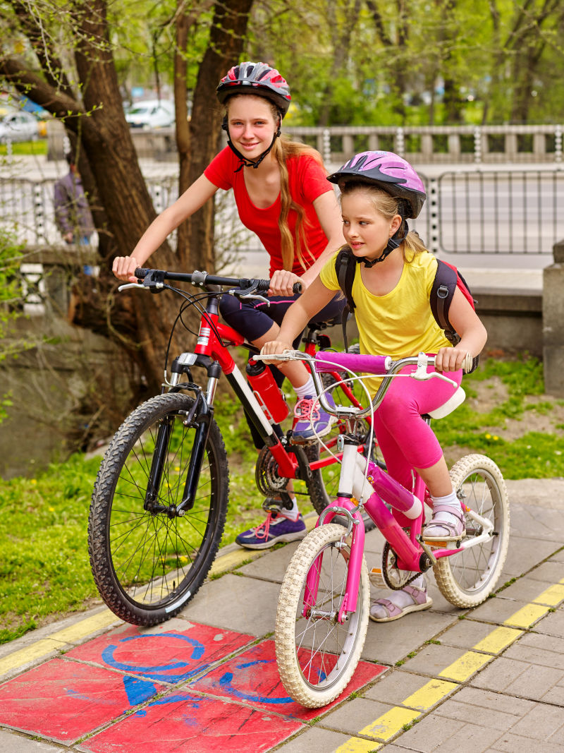 女孩们戴着自行车头盔背着帆布包骑着自行车女童在黄色自行车道上骑车自行车共享计划节省金钱和时间城市之旅