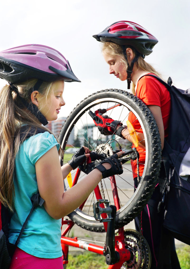 骑自行车的女孩女孩们戴着自行车头盔和自行车用手摇泵女孩给自行车轮胎打气儿童自行车修理