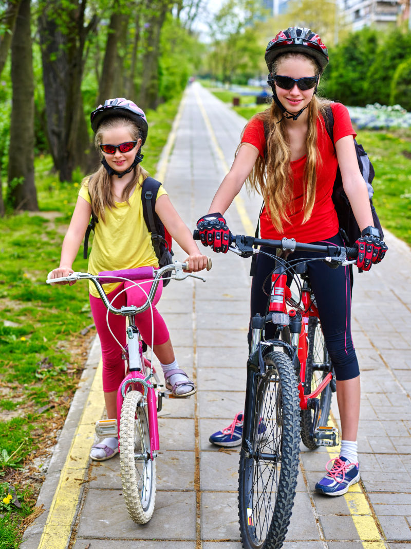 骑自行车的女孩女孩们戴着自行车头盔和玻璃背着帆布包骑着自行车女童在黄色自行车道上骑车自行车共享计划节省了城市街道的金钱和时间