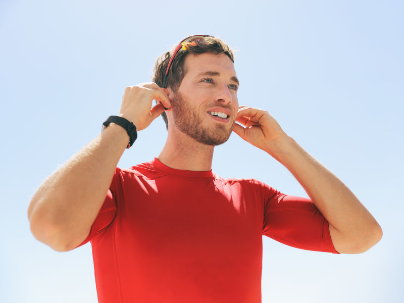年轻人戴上无线耳机蓝牙连接到智能手表耳机进行户外健身戴着耳塞进行锻炼的快乐活跃的人