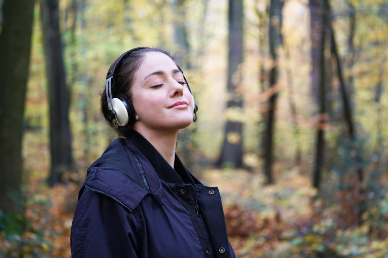 20多岁的年轻女子在森林里用无线耳机听音乐-秋天的户外生活方式-有复印空间