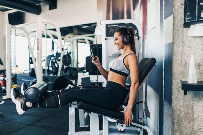 年轻健康迷人的女性在现代健身房锻炼用蓝牙耳机和智能手机听音乐