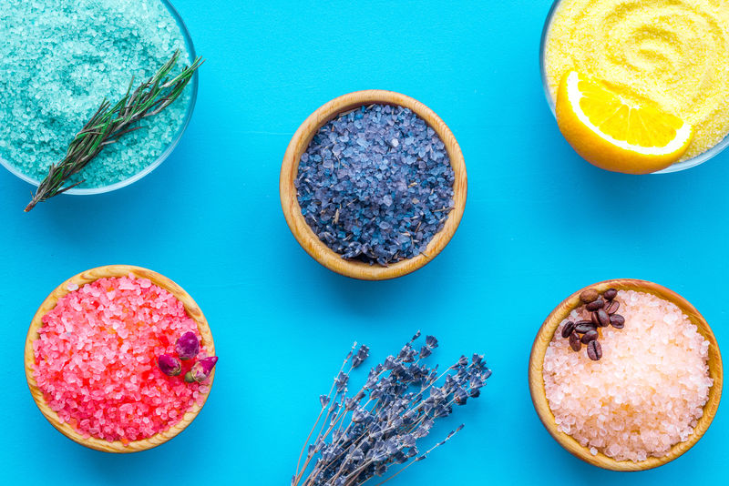 沐浴盐的香味-柠檬咖啡迷迭香玫瑰薰衣草-靠近碗-蓝色背景上有彩色浴盐-俯视图