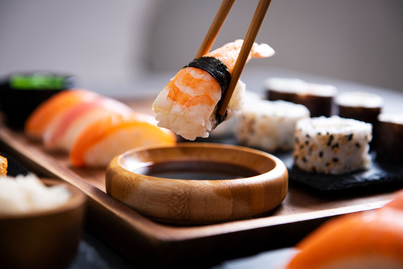 特写手拿着竹筷和黑子虾一起浸泡在酱油里-寿司的细节放在餐厅的木托盘上-手蘸酱油-日本料理理念