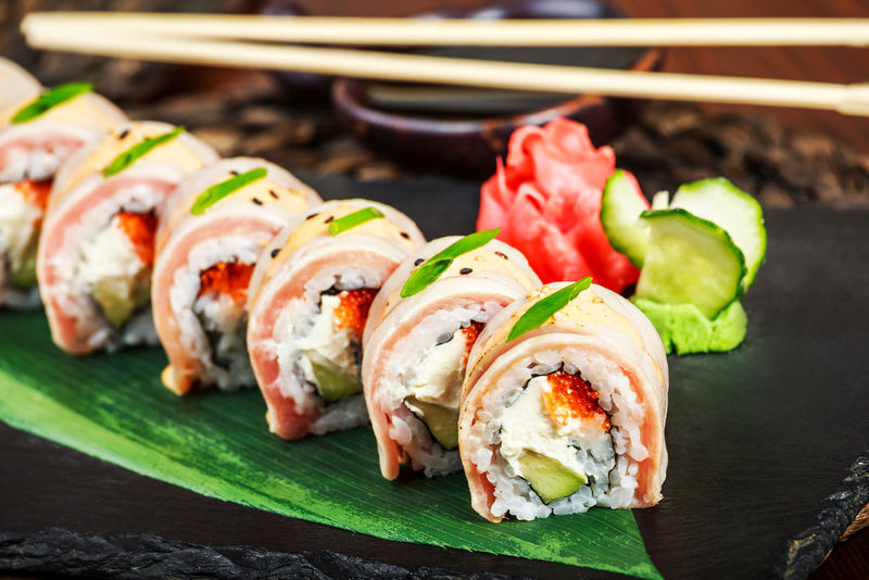 寿司卷上有三文鱼奶油奶酪红鱼子酱鳄梨和芥末-放在竹席上的黑石上-有选择性地聚焦-日本料理