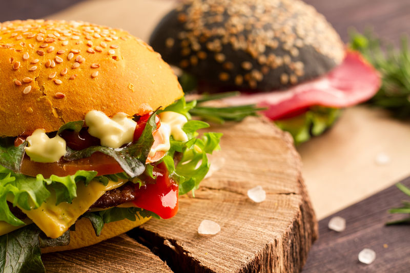多汁不健康的快餐汉堡-配牛肉切达干酪元素干酪生菜番茄沙司和番茄酱-配芝麻和喜玛拉雅盐的白面包-背景是一个黑色汉堡