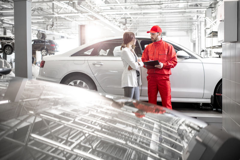 年轻女性客户-汽车修理工-穿着红色制服-在汽车服务部工作-具有复制空间的广角视图
