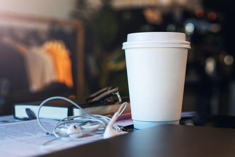 一张白纸咖啡杯的特写镜头放在空咖啡馆的桌子上没有人附近有耳机和笔记本模型