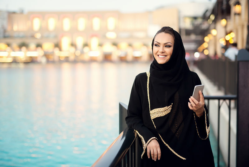 阿拉伯女人用智能手机打字微笑着一边看一边
