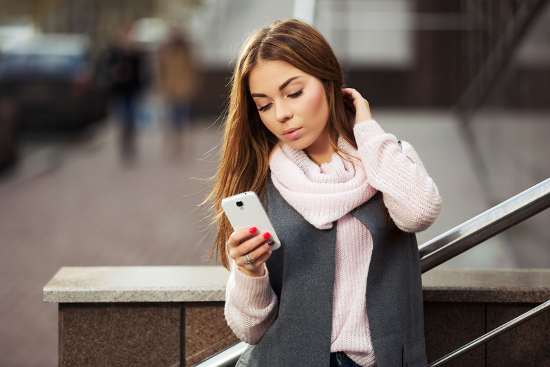 城市街头使用智能手机的年轻时尚女性