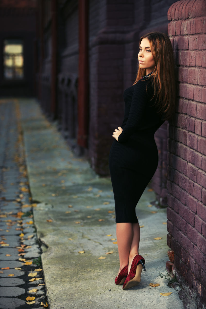 年轻的时尚女人在黑色的砖墙上穿黑色衣服