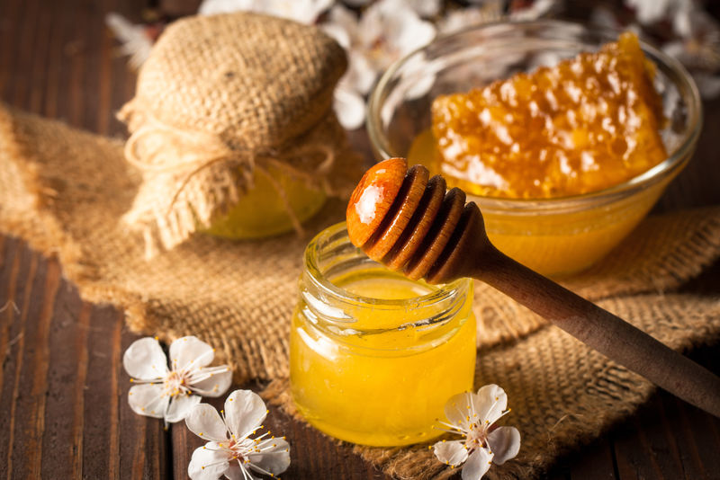 蜂蜜从木制的蜂蜜斗中滴到一个灰色的木制乡村背景的罐子里蜂胶和蜂蜜春季自然产品概念
