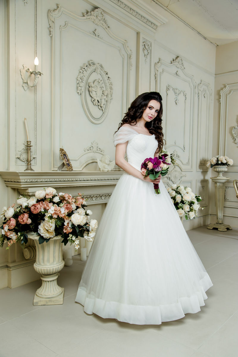 穿着豪华婚纱的漂亮新娘婚礼化妆和发型婚礼首饰华丽的婚礼花束紫兰花