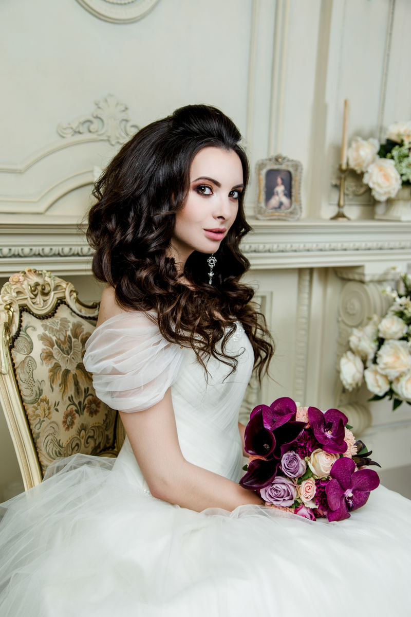 穿着豪华婚纱的漂亮新娘婚礼化妆和发型婚礼首饰华丽的婚礼花束紫兰花