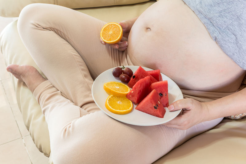 孕妇坐在沙发上拿着一盘水果