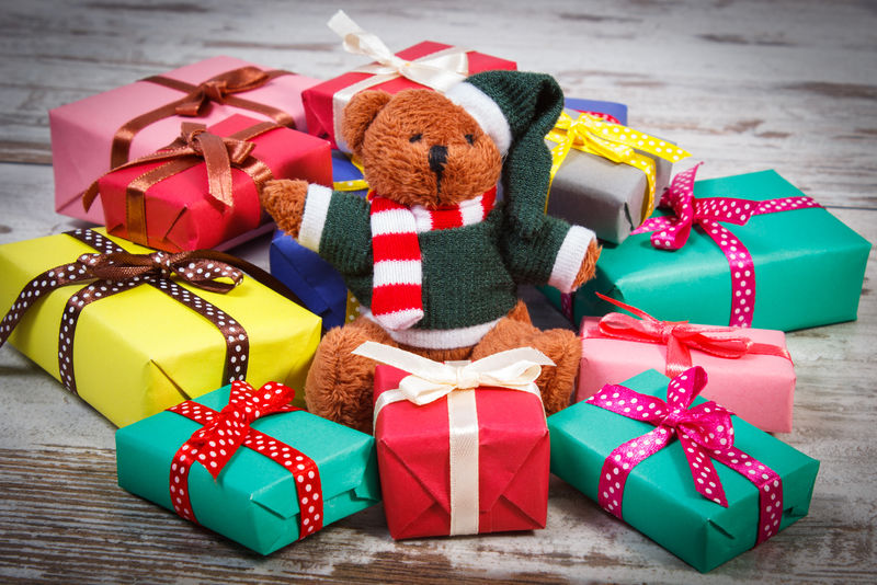 毛茸茸的泰迪熊和一堆五颜六色的圣诞礼物生日礼物情人节礼物或其他节日礼物-放在旧的木制白色桌子上