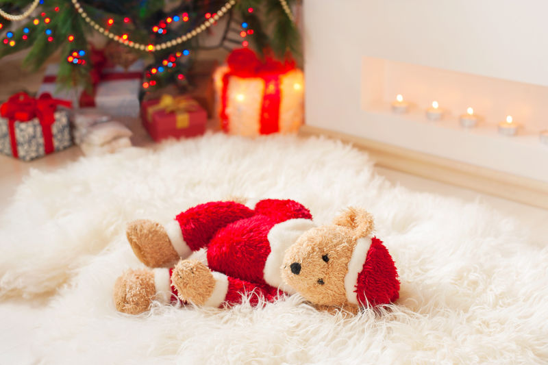 遗忘的礼物-圣泰迪熊玩具躺在羊皮地毯上-靠近被照亮的圣诞树-生动多彩的室内水平图像
