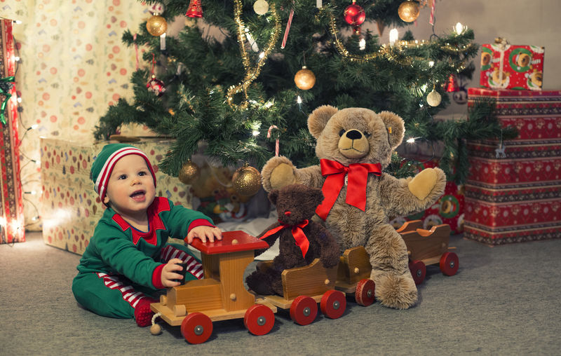 穿着精灵服装的婴儿在圣诞树下玩旧木火车和软玩具熊-复古