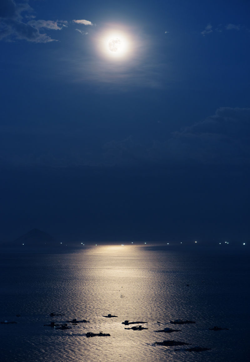 越南南海芽庄湾夜色中反射的满月-美丽神秘的月光照亮了海洋农场-在背景中可以看到岛屿和船只的灯光