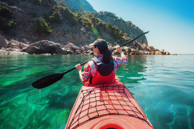 沿着岛上的岩石海岸在海上划艇的女人旅游