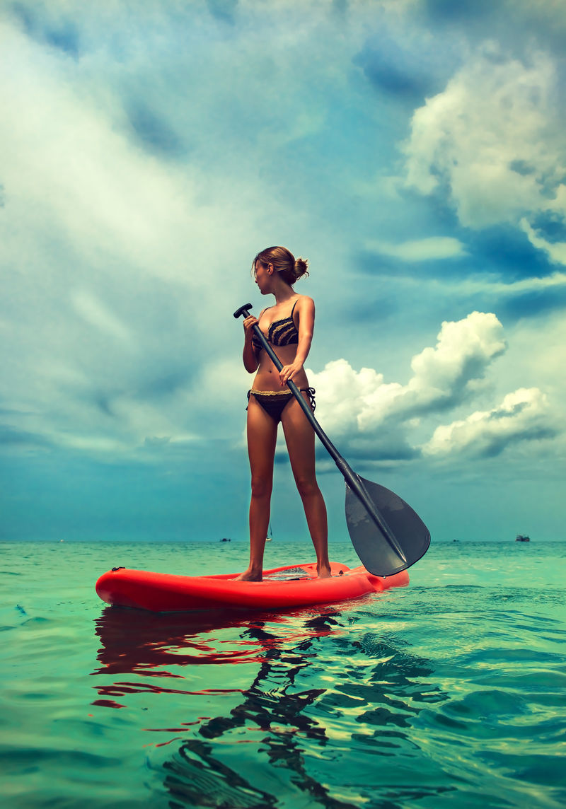 年轻苗条的女孩站在桨板在绿松石海SUP热带蓝色海洋泰国水上运动积极的生活方式