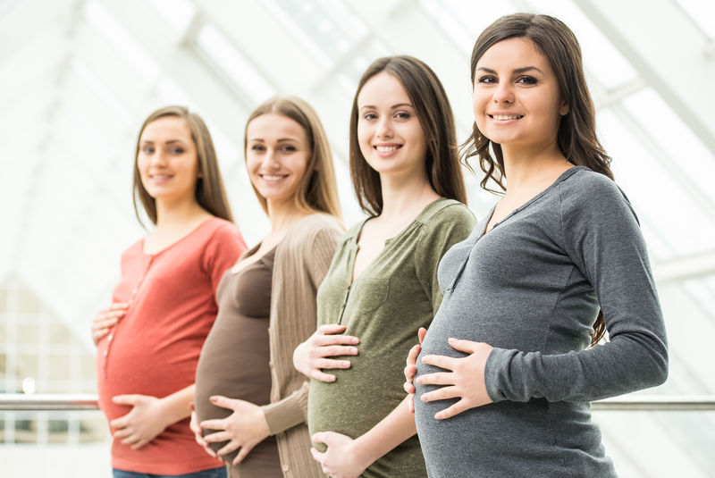四位微笑的孕妇用手触摸腹部的侧面图生育观念