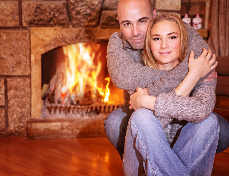 一对和蔼的夫妇坐在家里壁炉旁的画像浪漫的圣诞节庆典爱情和团聚的概念