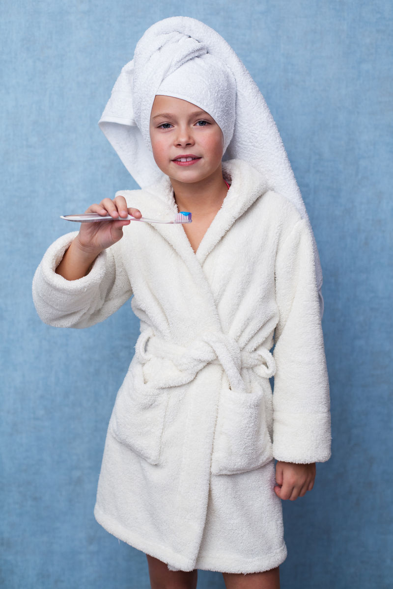 可爱的小女孩头上裹着毛巾手上拿着牙刷穿着浴袍准备刷牙蓝色背景