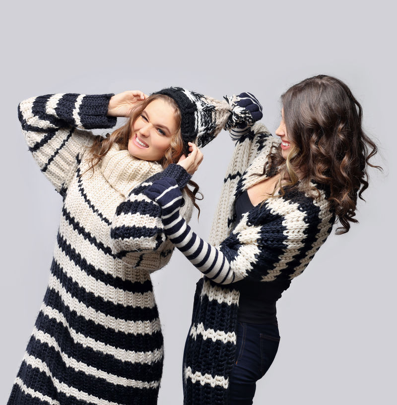 两个女孩戴着针织帽围巾毛衣和手套在蓝色背景下摆姿势