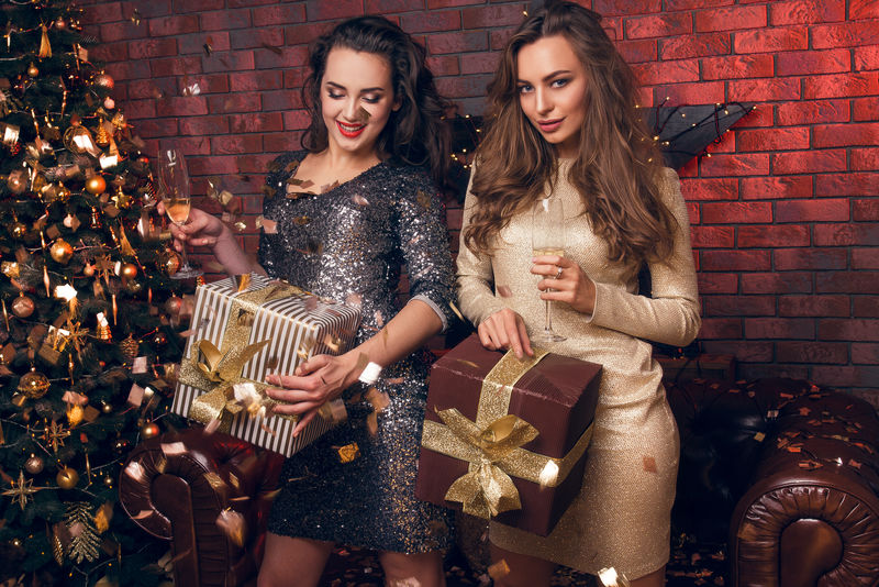 两个年轻漂亮有趣的女孩朋友微笑着玩拿着节日礼物喝着香槟跳舞圣诞晚会祝你2017年快乐！
