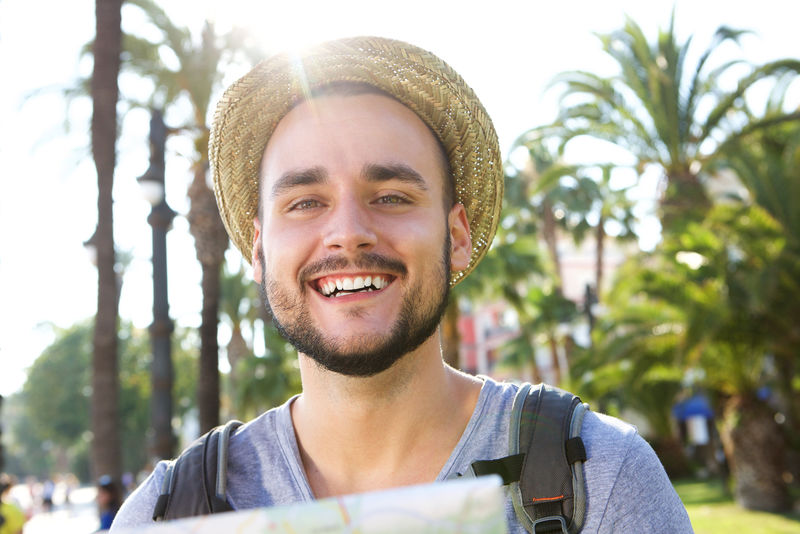 一个带着帽子和包站在外面微笑的旅行男子的肖像