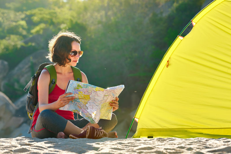 清晨年轻的女游客坐在帐篷旁阅读地图思考未来的徒步旅行亚洲旅游和积极的生活方式概念