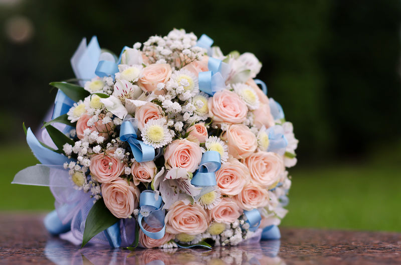美丽的新娘花束-粉红色的小玫瑰和蓝色丝带躺在公园绿草的背景上