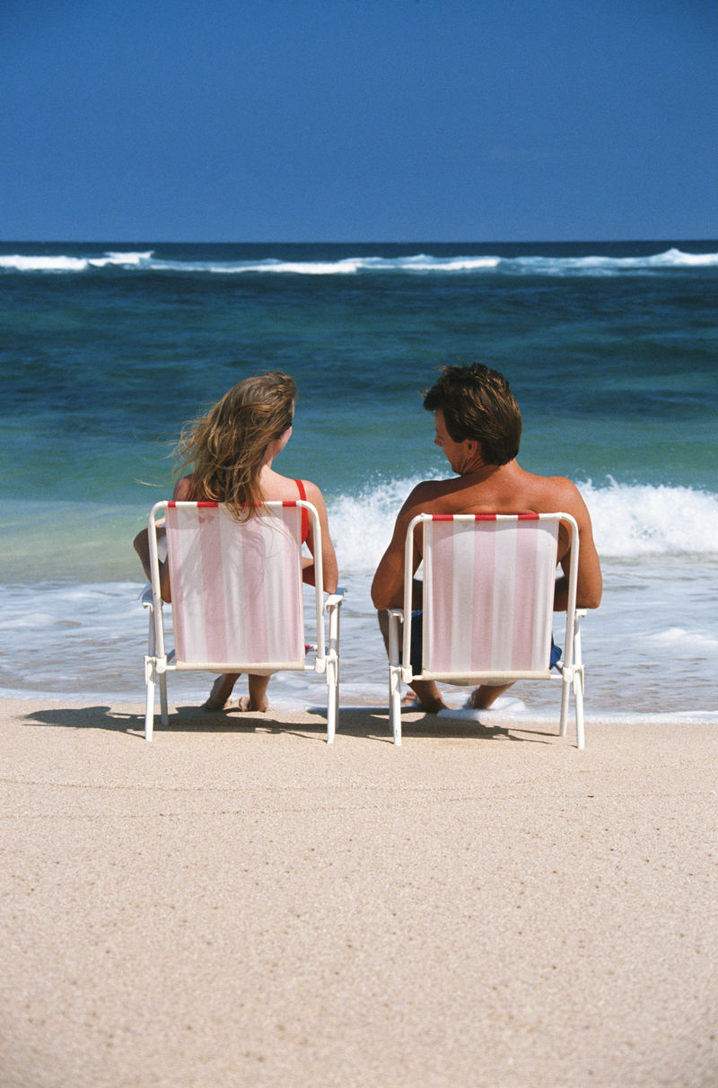 年轻夫妇坐在海边的沙滩椅上-看着水面