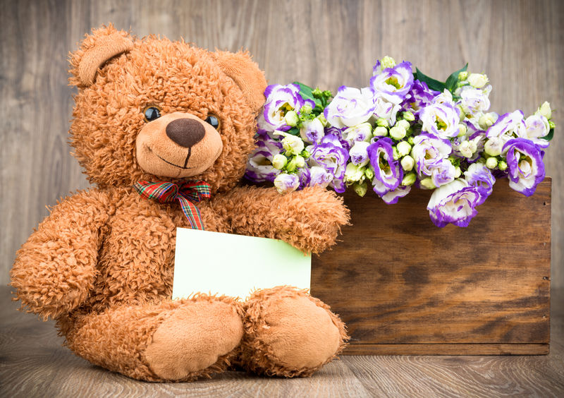 盒子里有漂亮的花和木制背景的泰迪熊