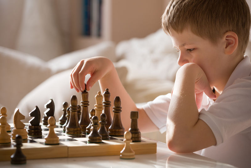 男孩在房间里下棋小聪明的男孩在家里下棋时集中精神思考